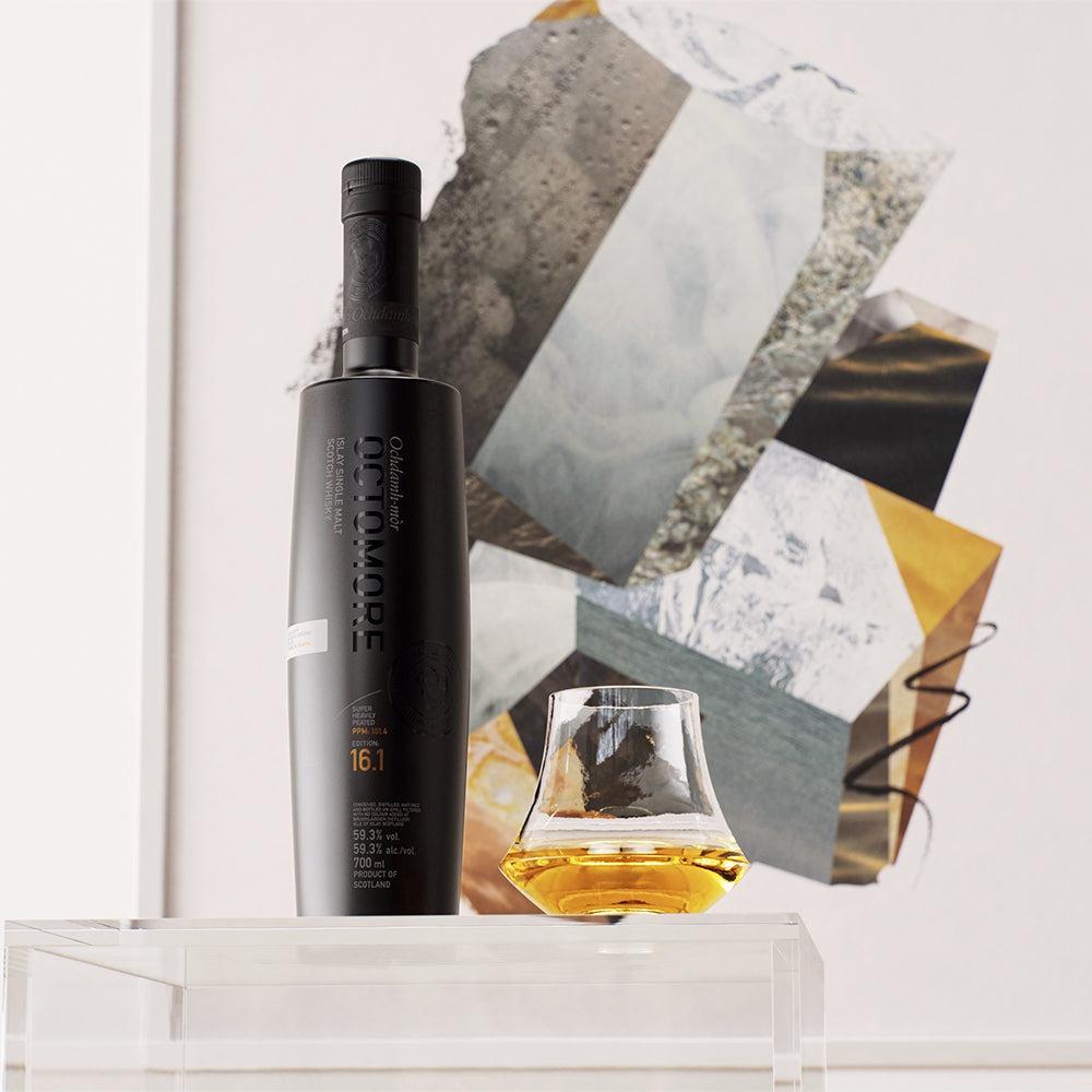 Zwarte fles Octomore 16.1 met een whiskyglas tegen een kunstwerk aan de muur