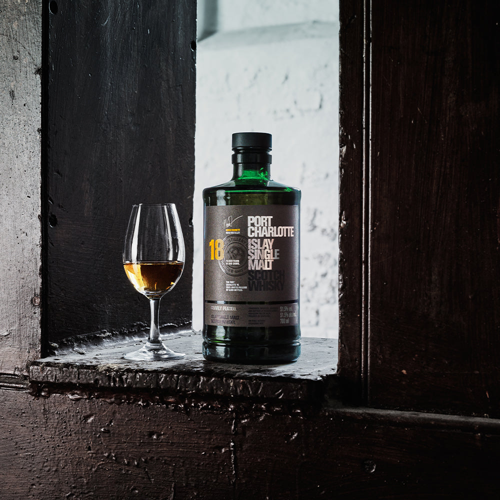Fles Port Charlotte 18 Islay single malt whisky naast een glas whisky op donker hout