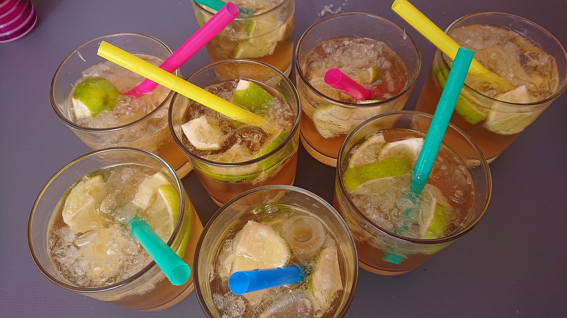 Acht glazen ginger ale met limoen, ijsblokjes en rietjes op een tafel