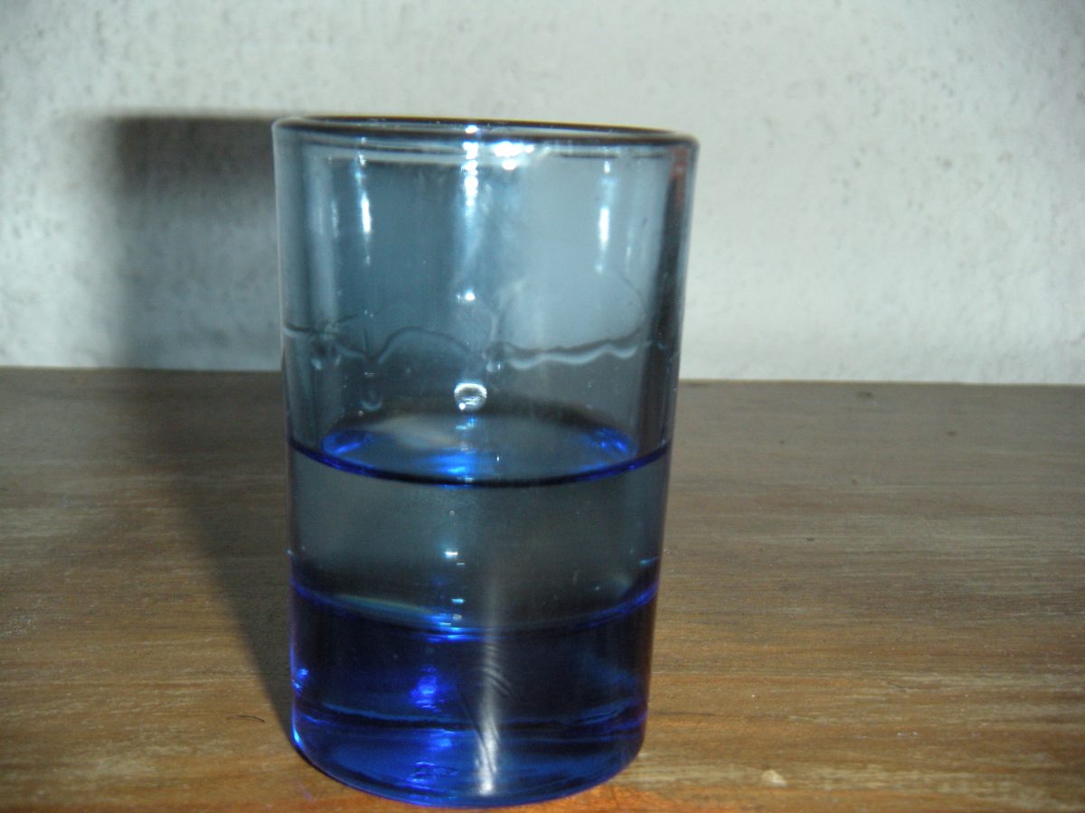 Een blauw glazen borrelglaasje met heldere drank op een houten tafel