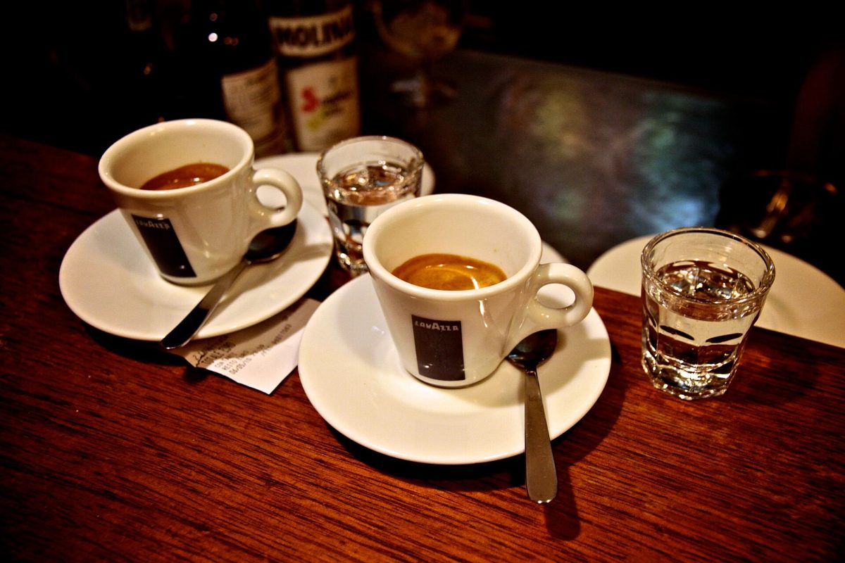 Twee kopjes espresso met lepels en een glas water op een houten cafetafel