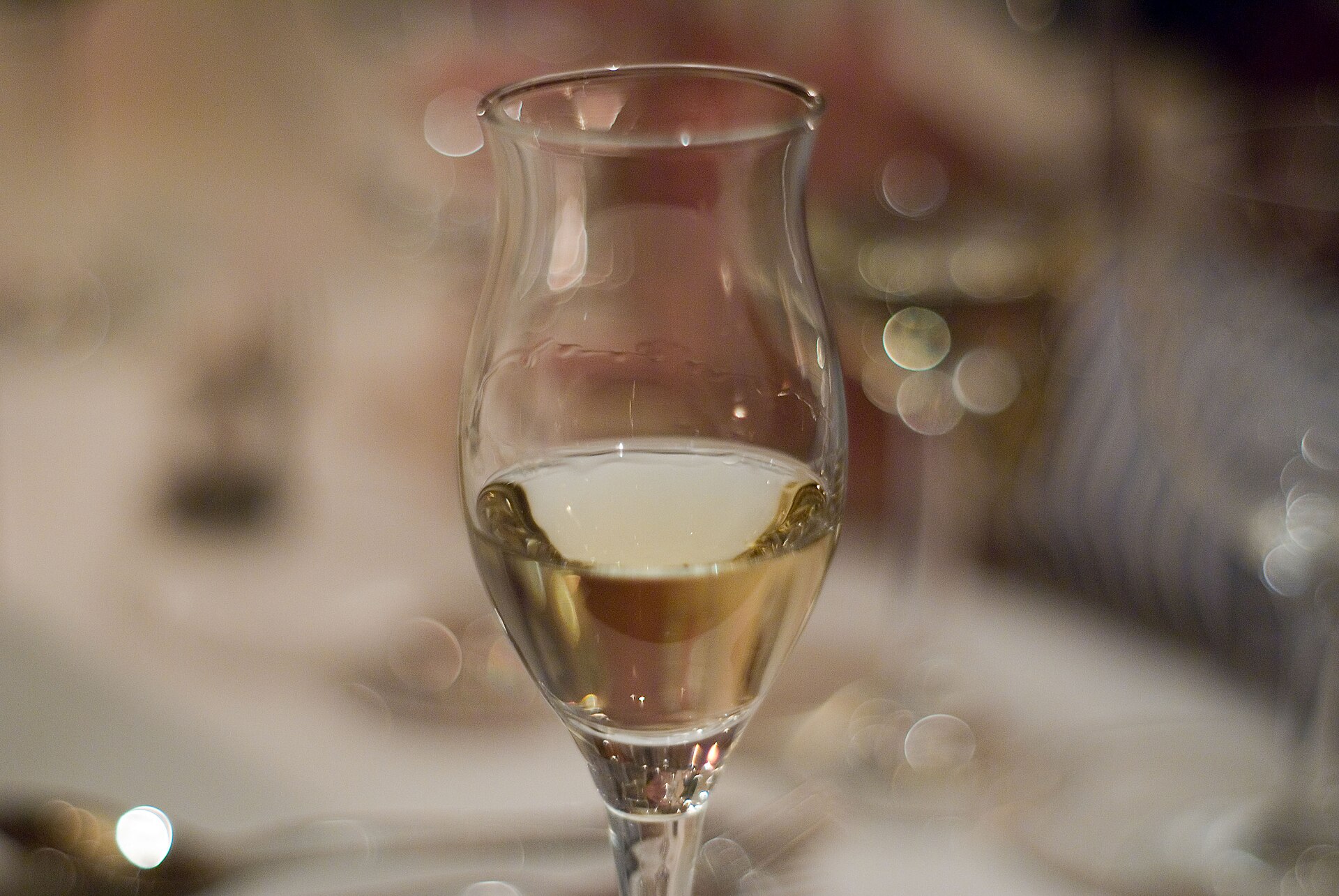 Een tulpvormig grappaglas op voet met een lichte grappa erin, op een gedekte tafel
