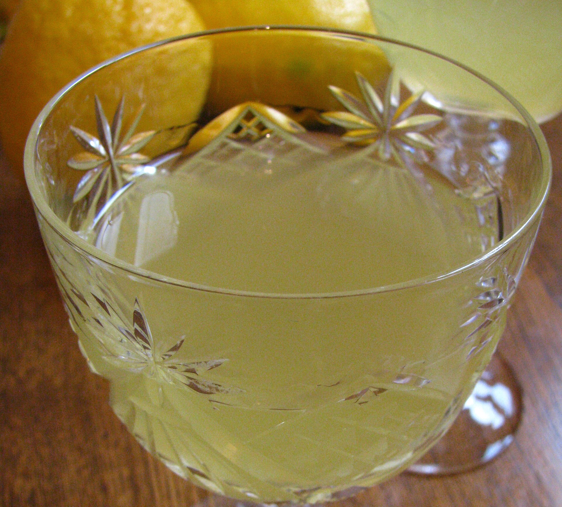 Een geslepen glas met limoncello, met hele citroenen erachter op tafel