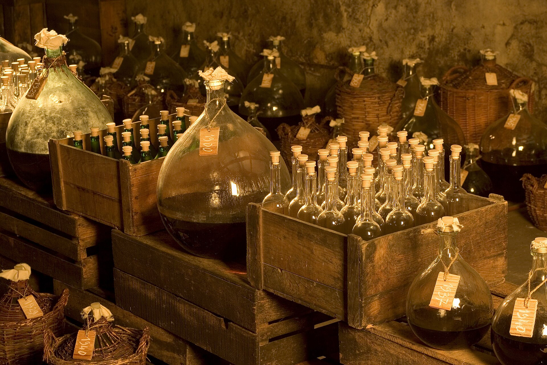 Glazen mandflessen en flessen armagnac met papieren labels in houten kisten in een donkere kelder