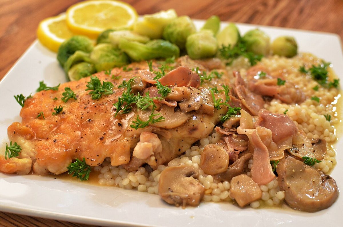 Kipfilet met een saus van paddenstoelen en marsala, met couscous en spruitjes op een bord