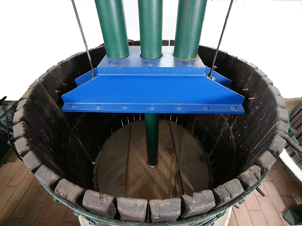 Een houten korfpers met een blauwe persplaat, van bovenaf gezien