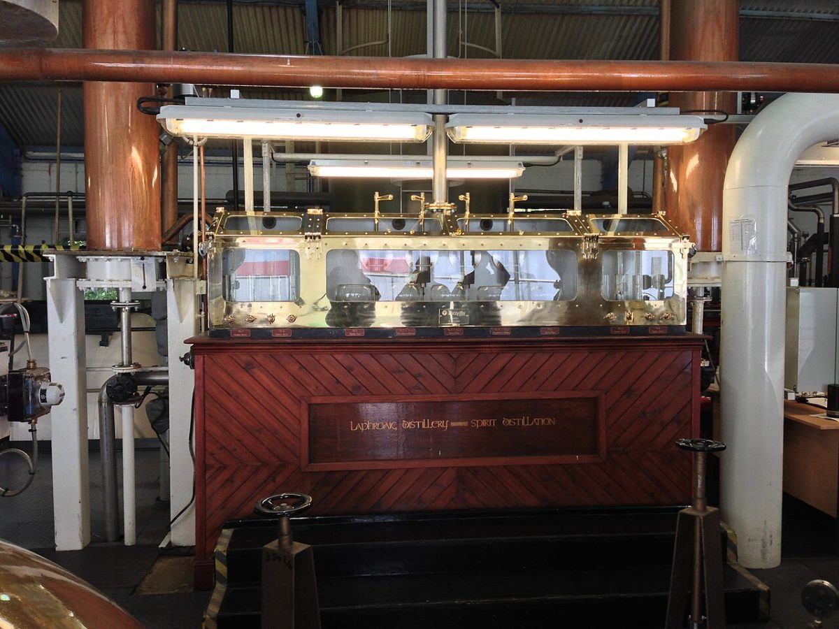 Een spirit safe van koper en glas in een houten kast tussen koperen leidingen in het stookhuis van Laphroaig