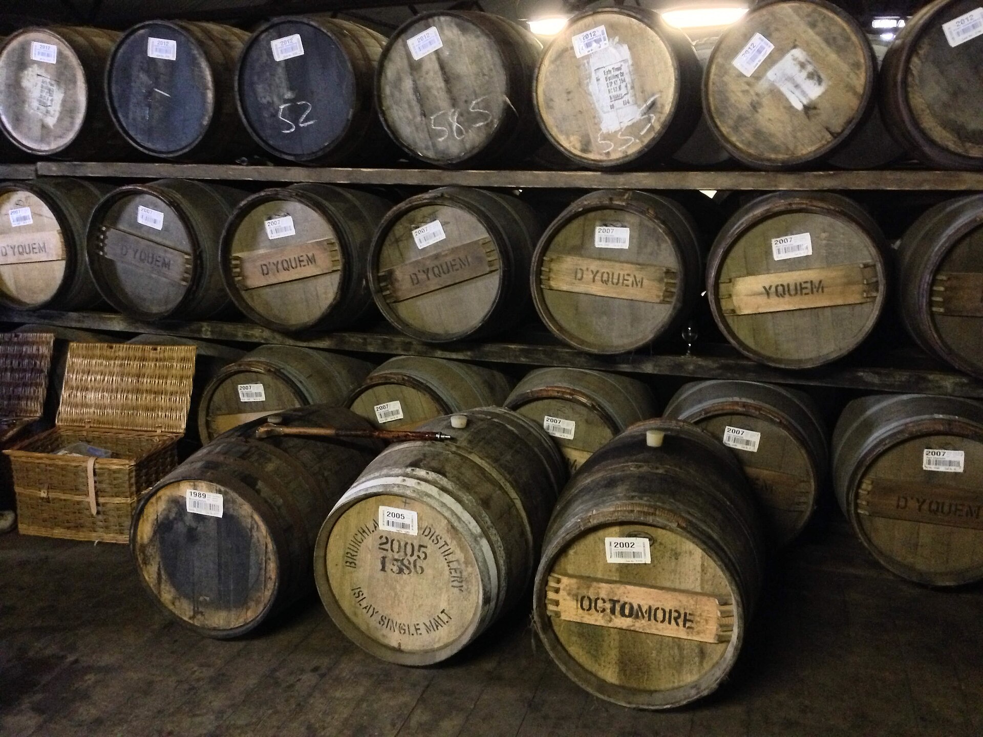 Rijen whiskyvaten op houten rekken in een donker pakhuis van Bruichladdich op Islay, een paar met Octomore op de bodem