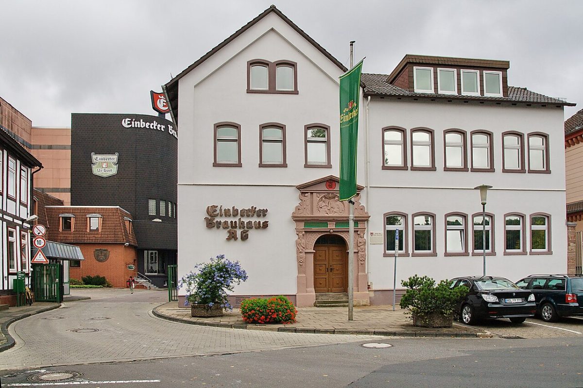 Het witte pand van het Einbecker Brauhaus aan een plein in Einbeck, met een groene vlag aan de gevel