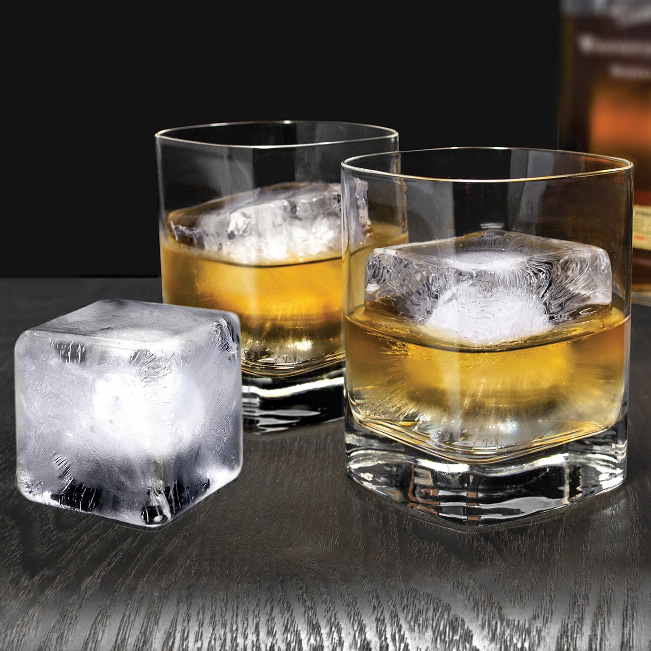 Twee tumblers met een bruine gedistilleerde drank en grote vierkante ijsblokken