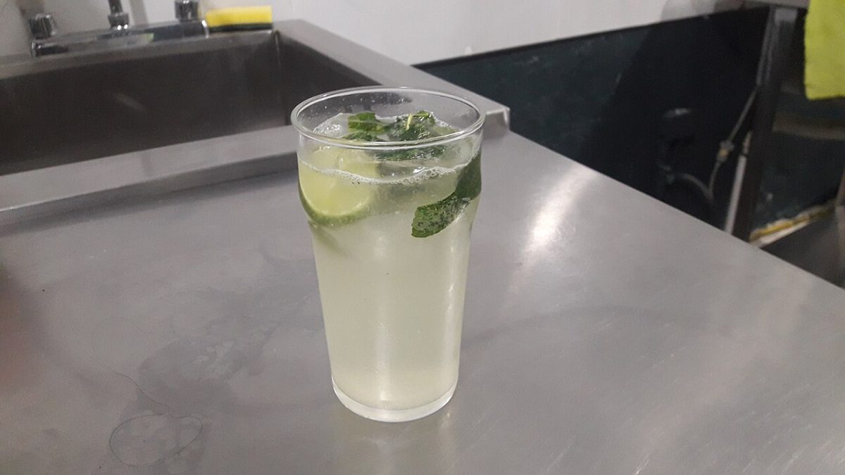Een hoog glas met een lichte drank, limoen en munt op een bar