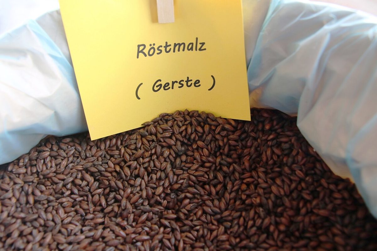 Een open zak donkere roostmout van gerst met een bordje Rostmalz erbij