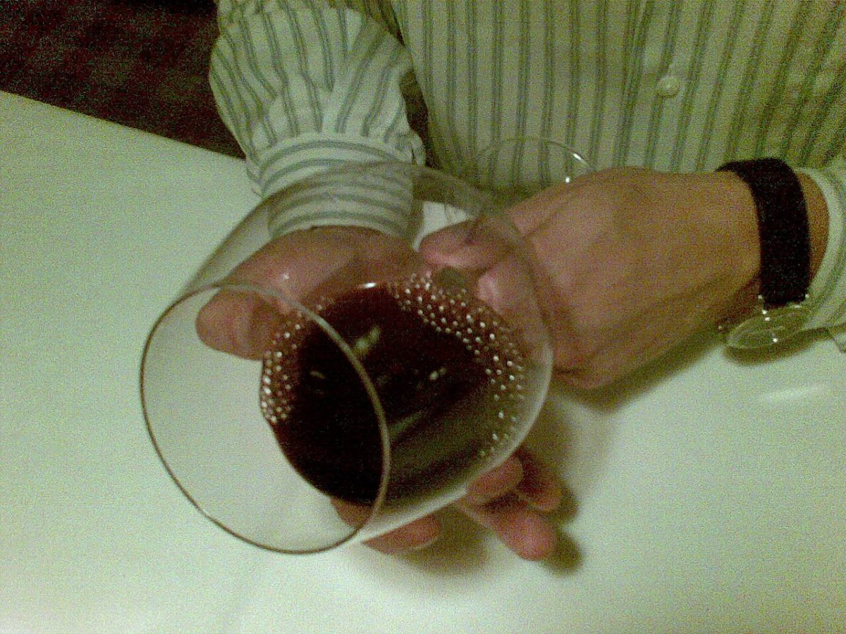Een hand die een glas rode wijn schuin houdt boven een wit tafelkleed