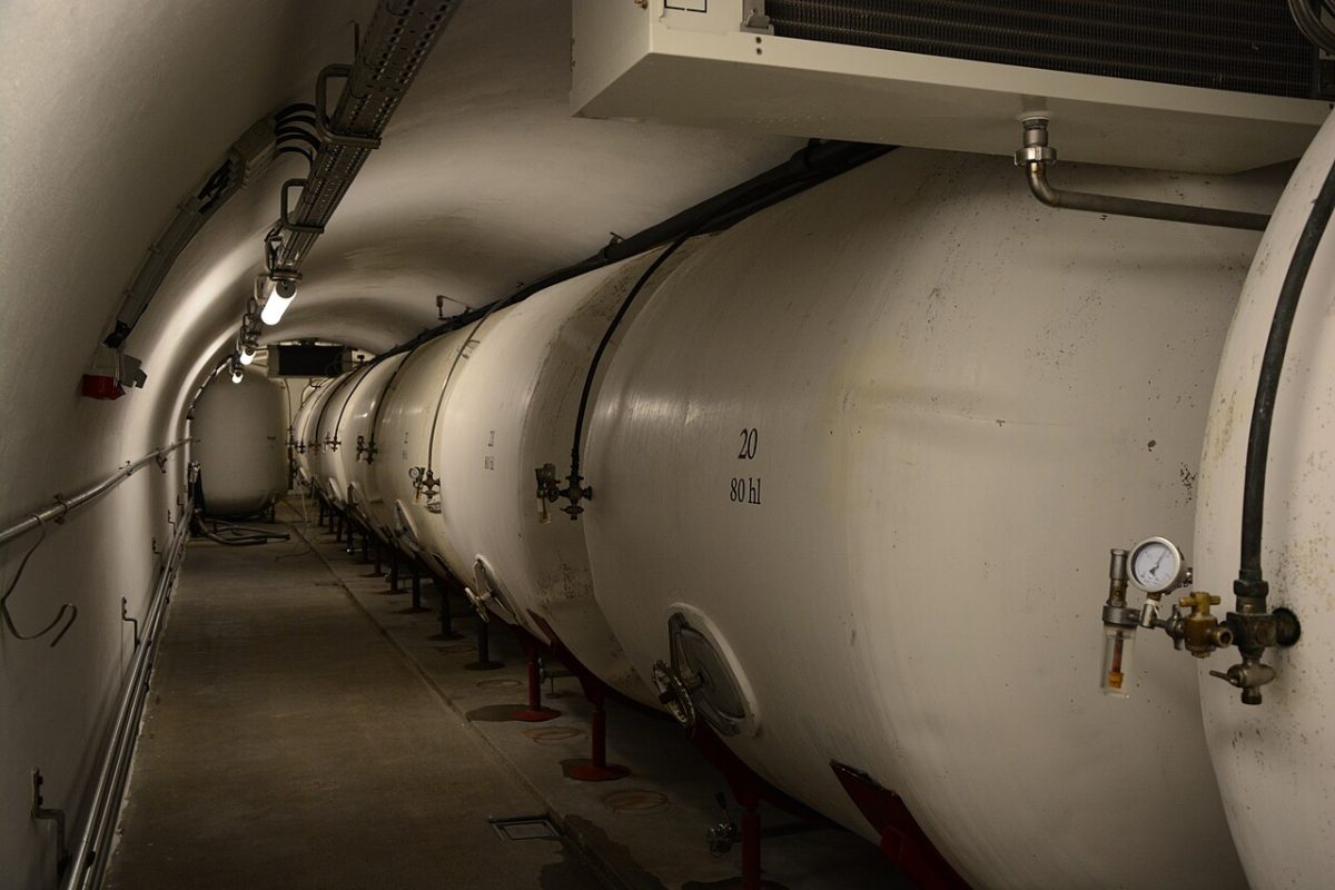 Een rij liggende lagertanks in een donkere brouwerijkelder
