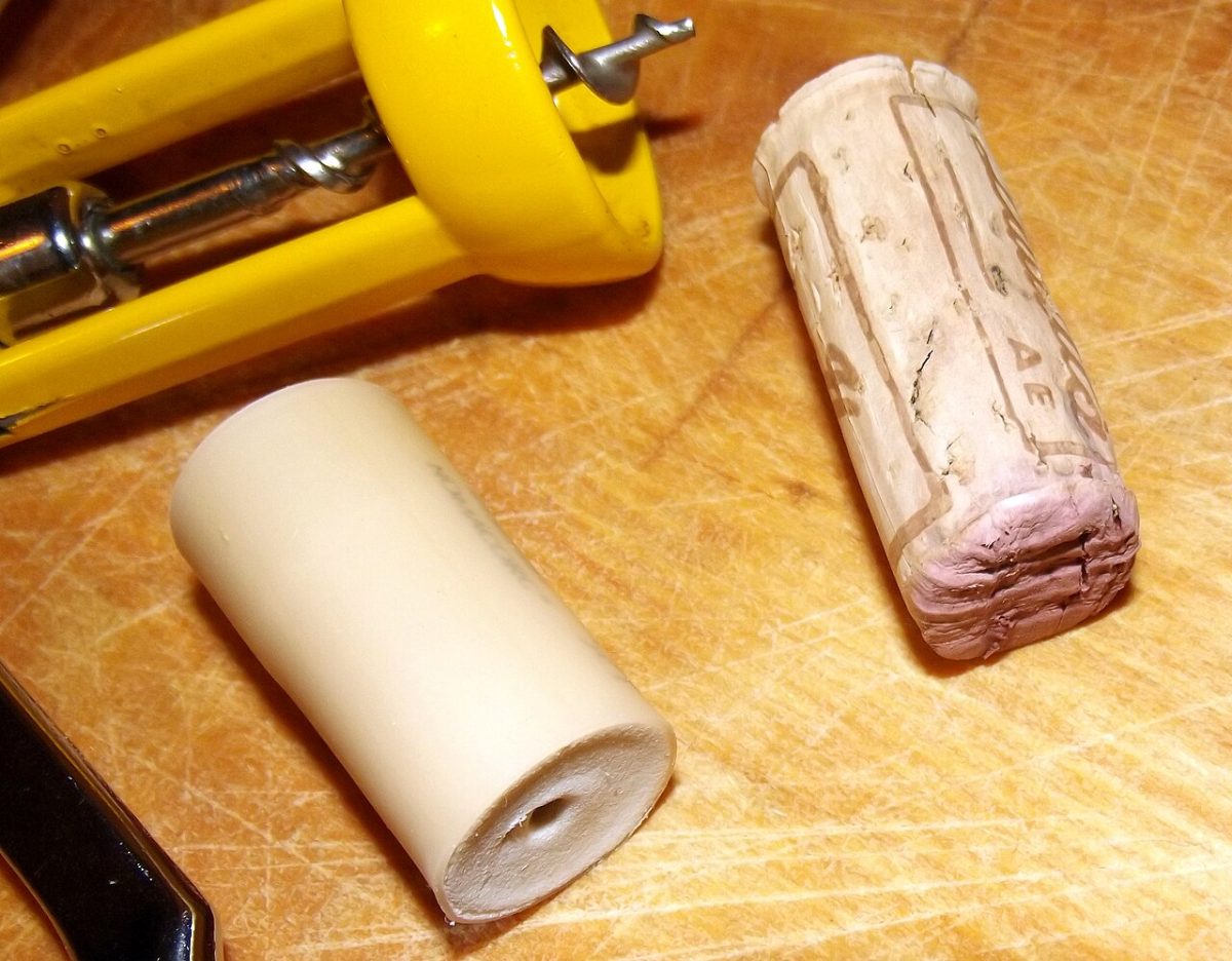 Een natuurkurk met wijnvlek naast een gladde kunststofstop op een houten plank