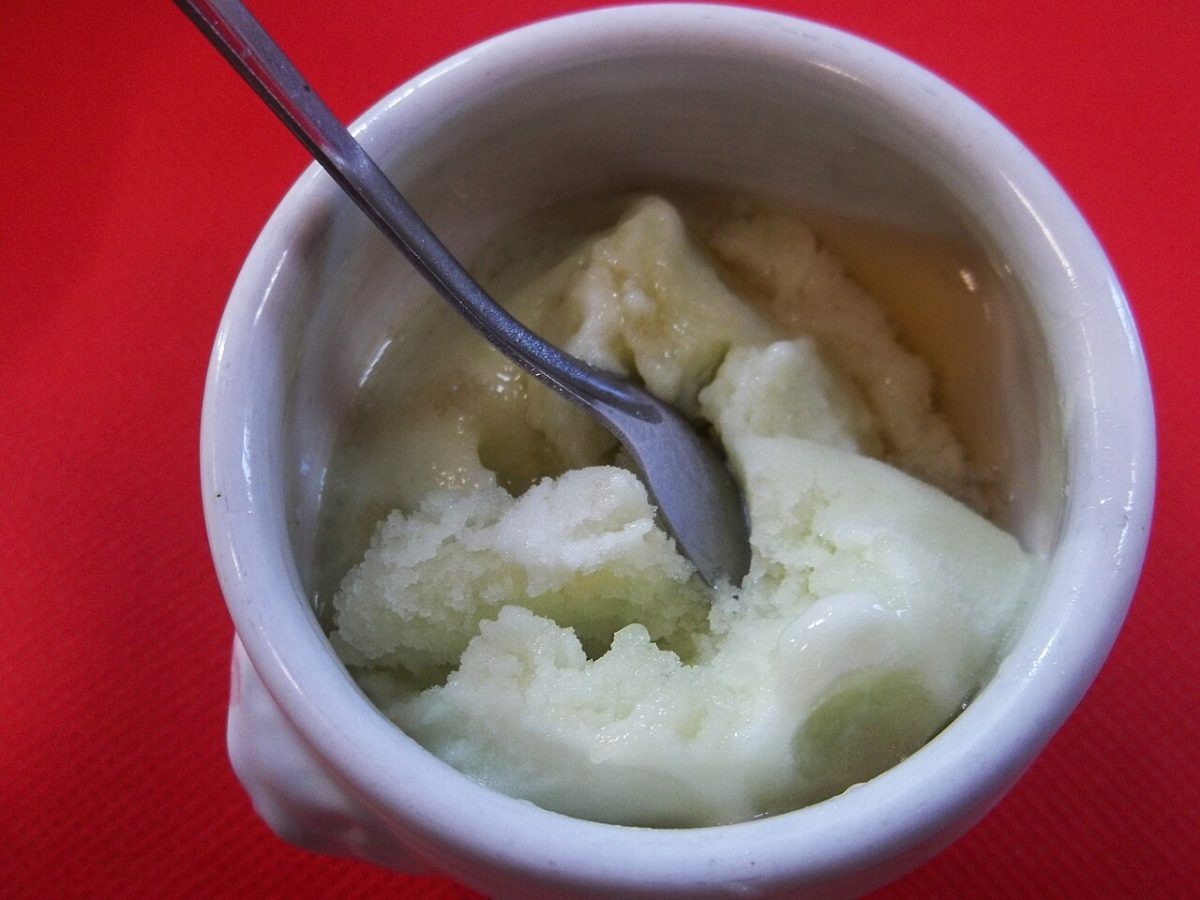 Ein weißes Schälchen mit Apfelsorbet und einem Löffel, mit klarer Spirituose am Rand