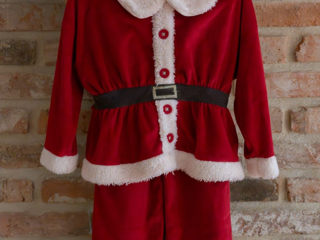 A red costume with white fur trim and a black belt, hanging from a beam against a brick wall