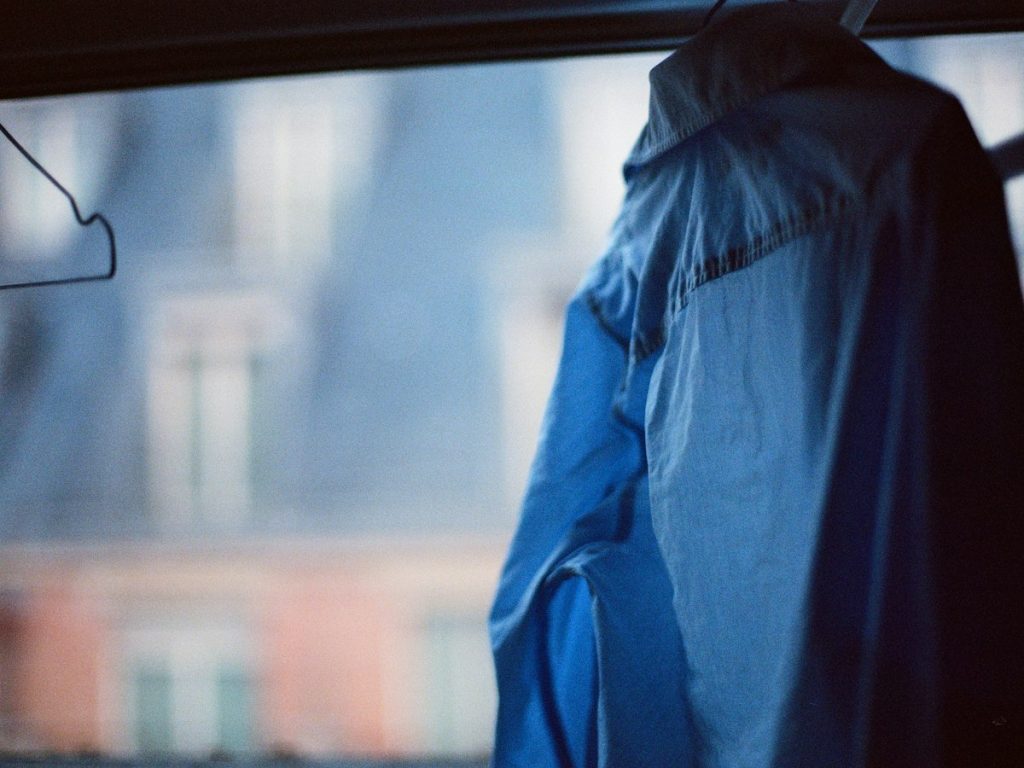 A blue raincoat on a hanger in front of a window