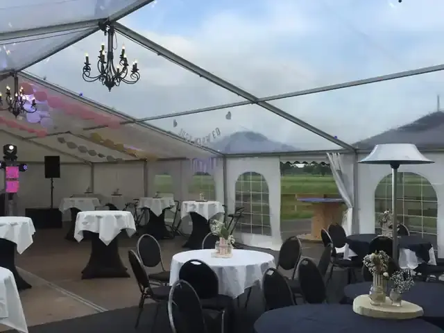 Transparante tent met een kroonluchter, ronde tafels en statafels