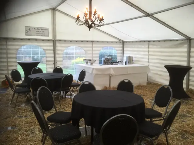 Tent met ronde tafels, zwarte stoelen, een koffietafel en een kroonluchter