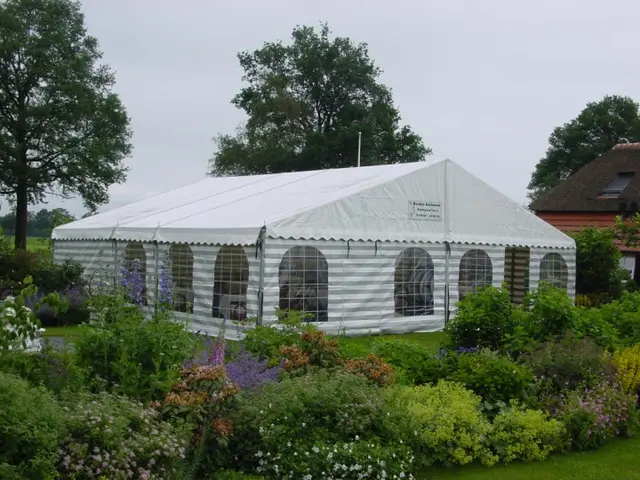 Partytent van 8 meter breed met witte zeilen in een tuin vol bloemen